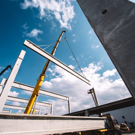 Construction site of prefabricated hall with cement pillars and concrete beams moving crane