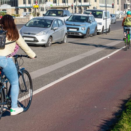 People cycling on a cycle path next to cars